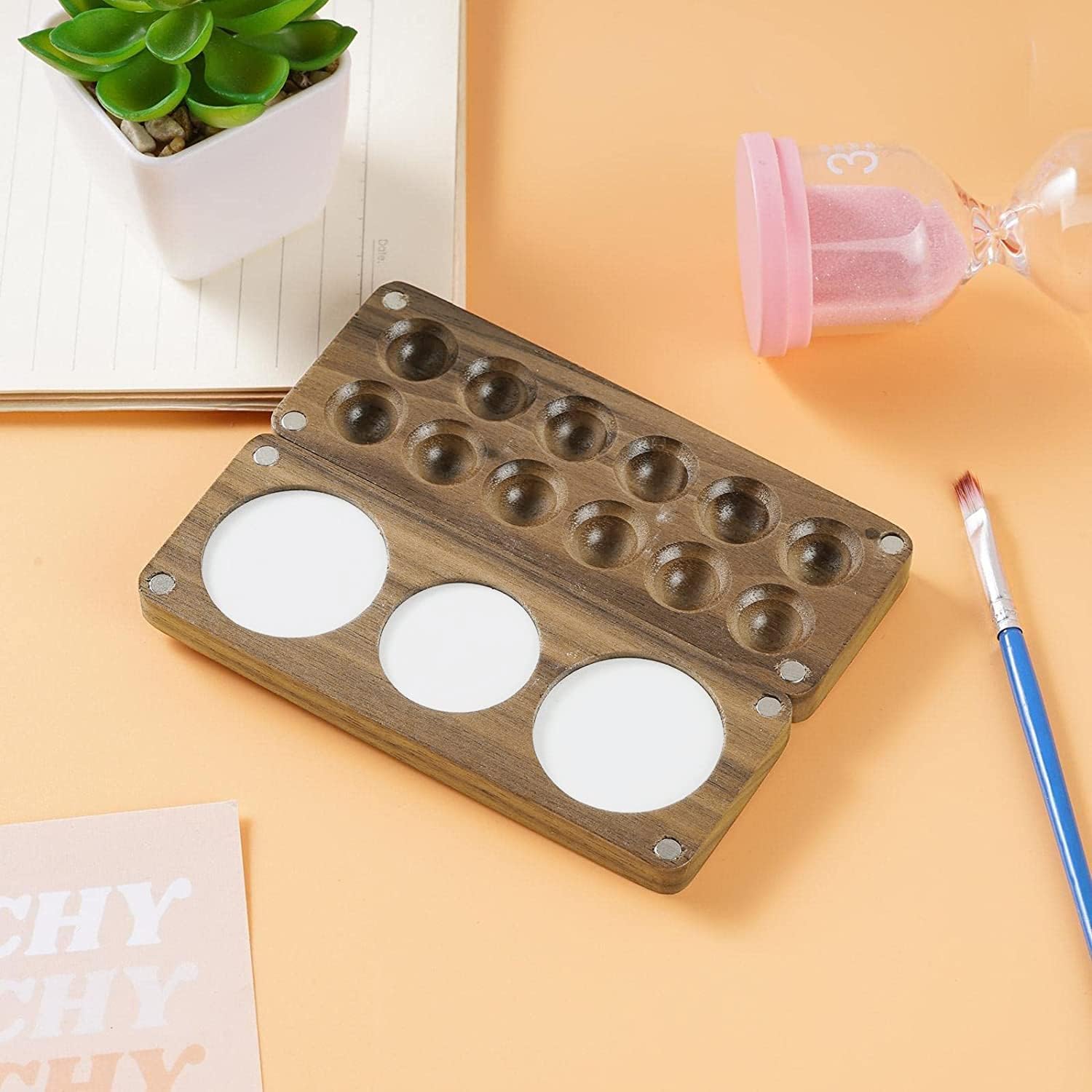 Portable 12-round wooden palette attached to sketchbook with clip, ideal for travel and outdoor painting.