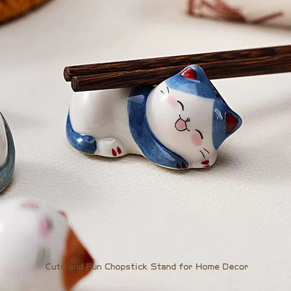 Ceramic cat chopstick rests holding chopsticks, forks, spoons, and paint brushes on dining table
